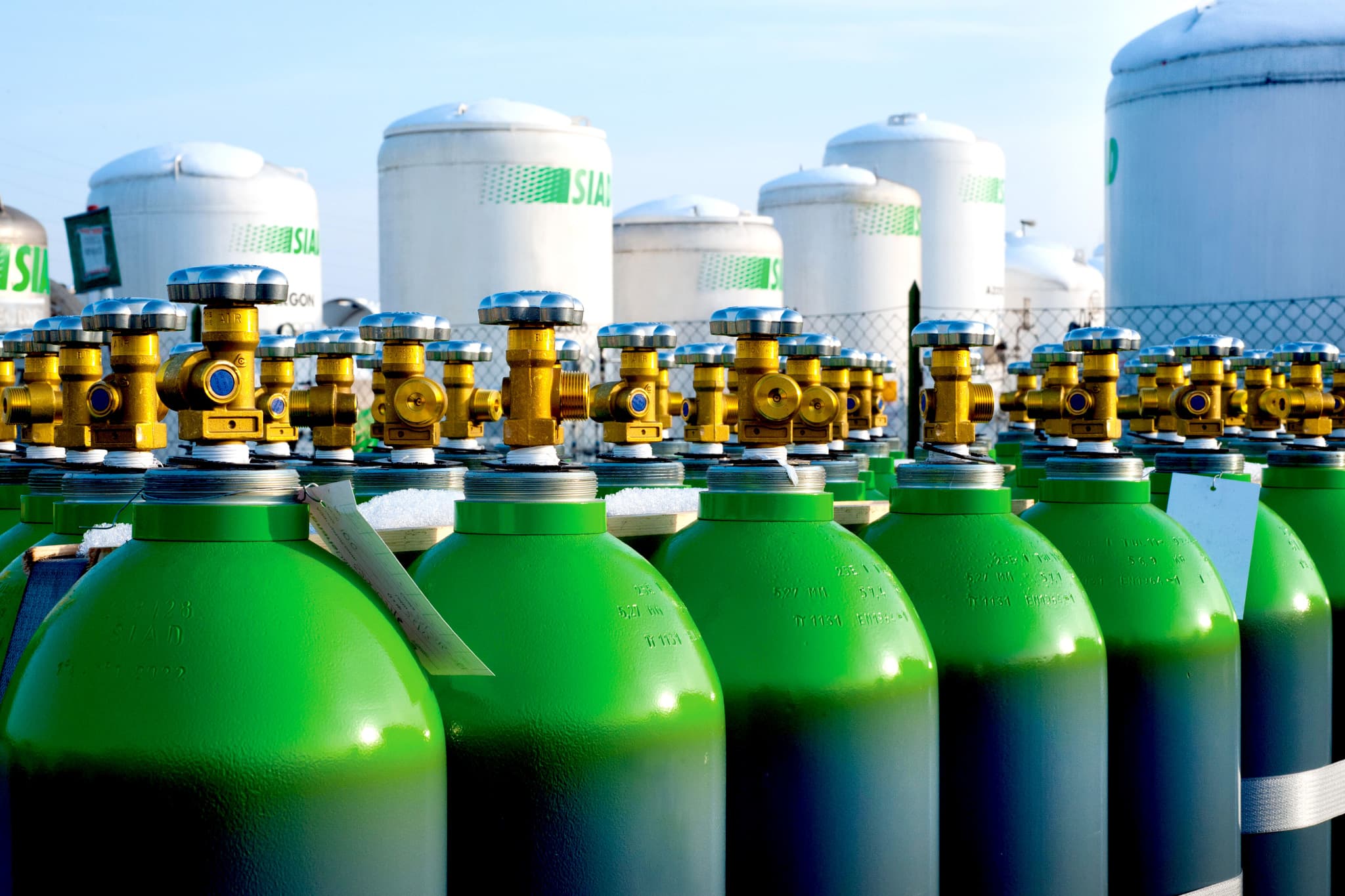 Green industrial gas cylinders with brass valves in front of SIAD storage tanks.