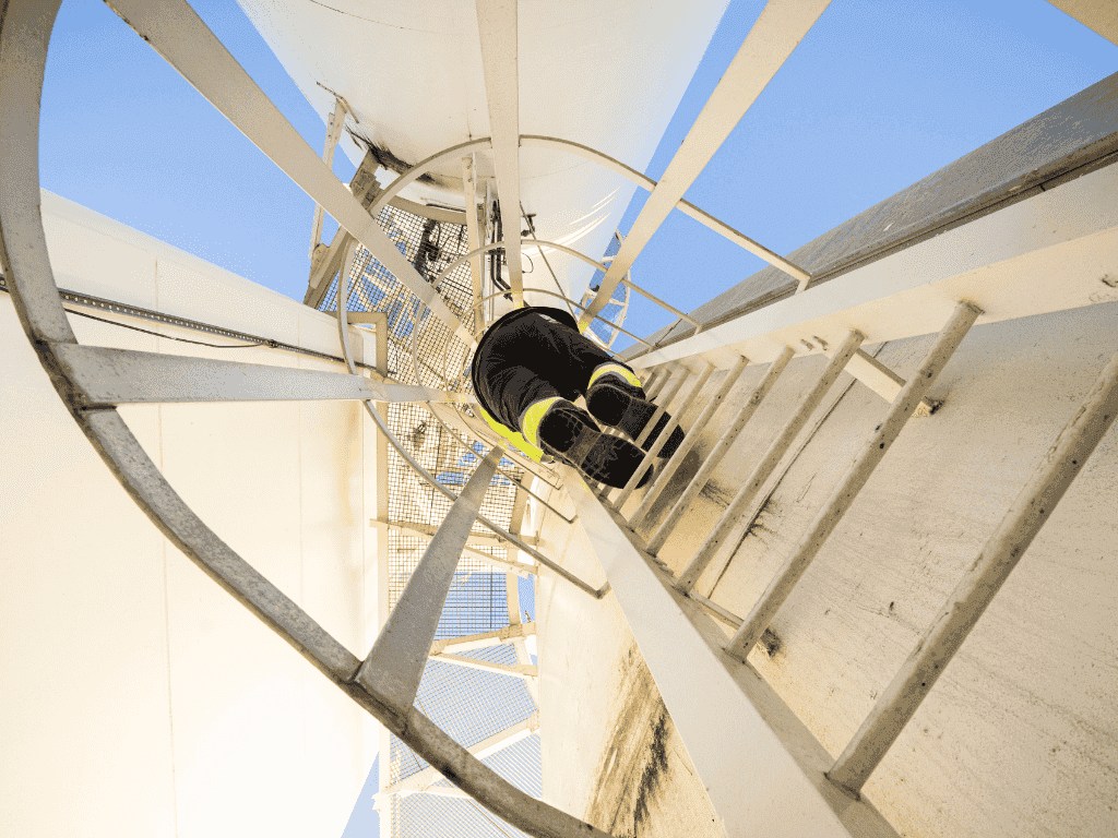 Worker climbing a vertical industrial ladder inside a metal structure under clear blue sky